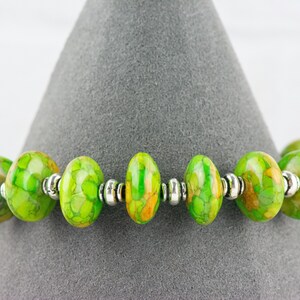 Pode incluir: Um bracelete com padr&atilde;o verde e amarelo com contas prateadas.