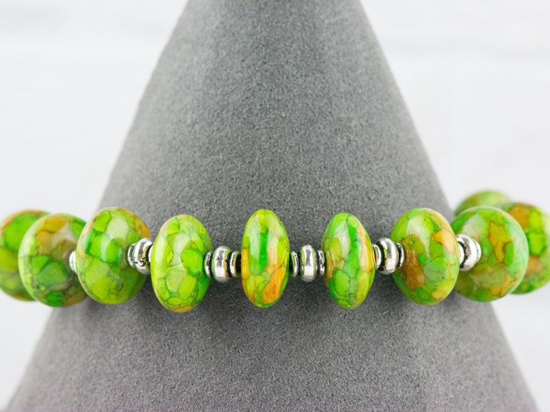 Pode incluir: Um bracelete com padr&atilde;o verde e amarelo com contas prateadas.