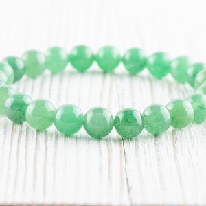 May include: A green gemstone bracelet made of round beads. The bracelet is on a white wooden surface.