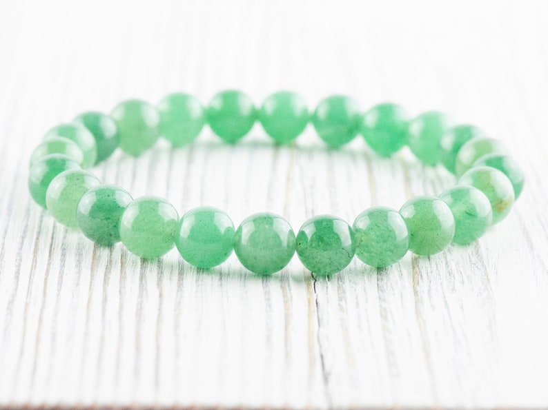May include: A green gemstone bracelet made of round beads. The bracelet is on a white wooden surface.