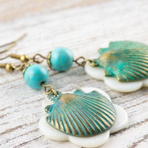 May include: A pair of turquoise and gold shell earrings with white accents. The earrings feature a seashell design with a turquoise and gold finish, and are accented with white.
