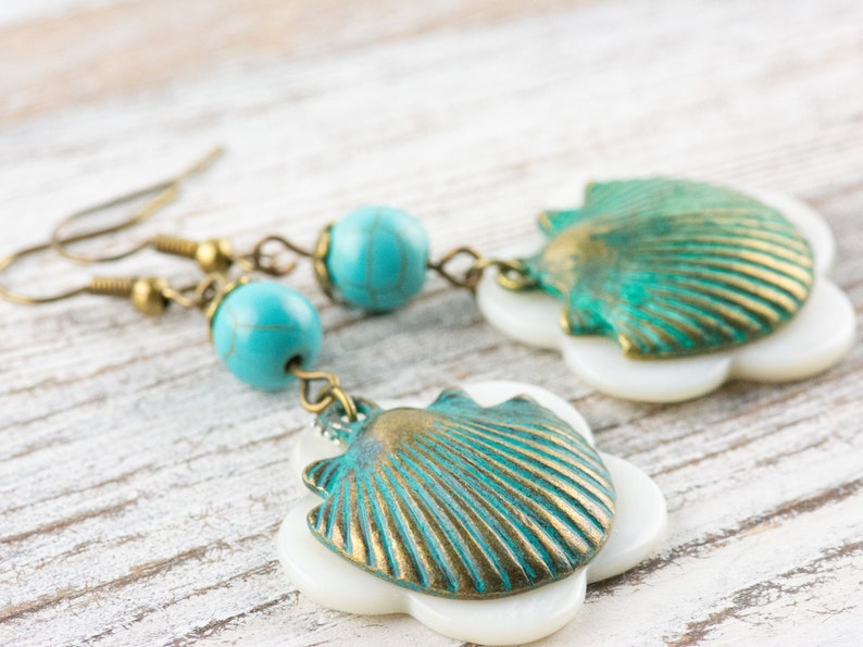 May include: A pair of turquoise and gold shell earrings with white accents. The earrings feature a seashell design with a turquoise and gold finish, and are accented with white.