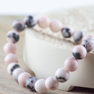 May include: A pink and black gemstone bracelet with round beads. The bracelet is made of natural stones and is a beautiful and unique piece of jewelry.