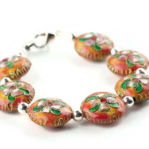 May include: A bracelet made of round, orange beads with floral designs in pink, green, and white. The beads are connected by silver metal links.