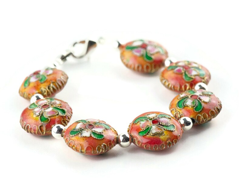 May include: A bracelet made of round, orange beads with floral designs in pink, green, and white. The beads are connected by silver metal links.