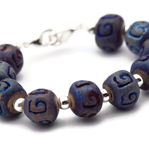 Pu&ograve; includere: Un braccialetto blu e argento con una serie di perline rotonde. Ogni perlina ha un motivo a spirale inciso sulla sua superficie.