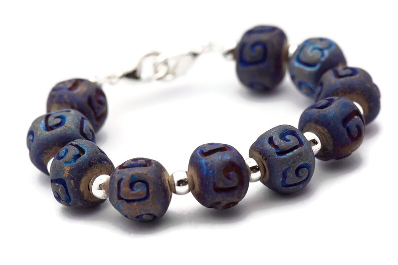 Pu&ograve; includere: Un braccialetto blu e argento con una serie di perline rotonde. Ogni perlina ha un motivo a spirale inciso sulla sua superficie.