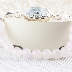 Puede incluir: Un reloj plateado con una esfera blanca y una pulsera de cuentas de cuarzo rosa.
