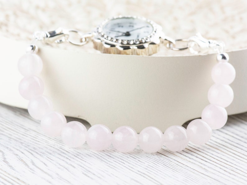Puede incluir: Un reloj plateado con una esfera blanca y una pulsera de cuentas de cuarzo rosa.