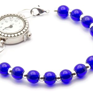 May include: A silver pocket watch with a white face and black numbers is attached to a bracelet made of blue glass beads and silver spacers.