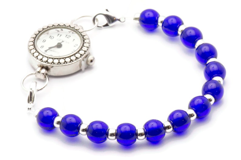 May include: A silver pocket watch with a white face and black numbers is attached to a bracelet made of blue glass beads and silver spacers.