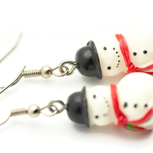 May include: A pair of silver snowman earrings with red and white accents. Each snowman has a black top hat and a red scarf.