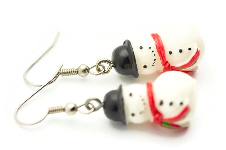 May include: A pair of silver snowman earrings with red and white accents. Each snowman has a black top hat and a red scarf.