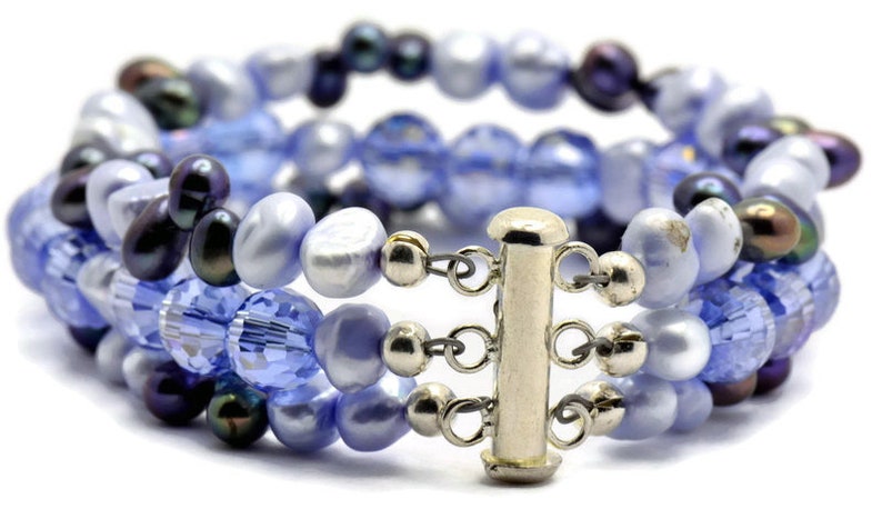 May include: A multi-strand bracelet with a silver clasp. The bracelet is made of blue and purple glass beads and pearls.