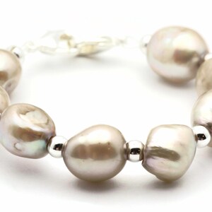 Peut inclure: Un bracelet en perles avec des accents argent&eacute;s. Le bracelet pr&eacute;sente une s&eacute;rie de grosses perles de forme irr&eacute;guli&egrave;re de couleur gris clair.