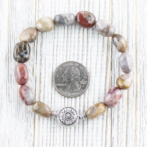 Op de afbeelding: Een armband gemaakt van bruine, grijze en roze stenen met een zilveren bedel. De armband is ongeveer zo groot als een Amerikaanse kwart.