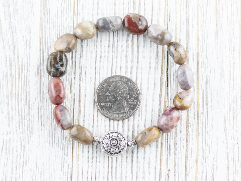Op de afbeelding: Een armband gemaakt van bruine, grijze en roze stenen met een zilveren bedel. De armband is ongeveer zo groot als een Amerikaanse kwart.