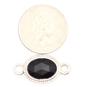 May include: Silver oval connector with a black faceted gemstone. The connector has two loops for attaching jewelry.