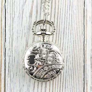 May include: A silver pocket watch with a floral design on the face and a chain attached.