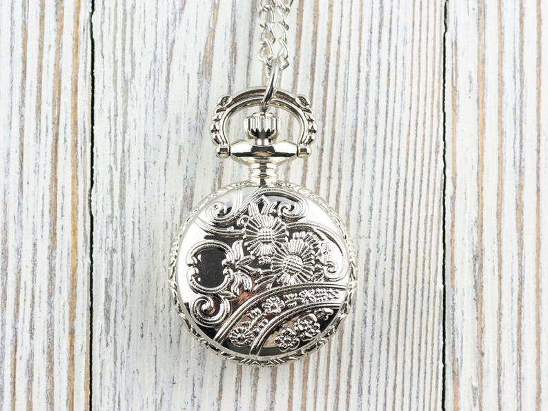 May include: A silver pocket watch with a floral design on the face and a chain attached.