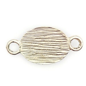 May include: Silver oval charm with a textured surface and two loops on either side.