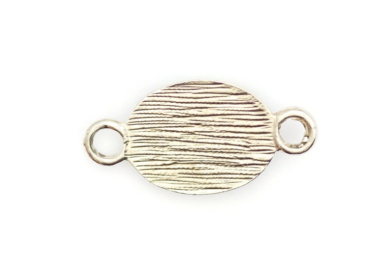 May include: Silver oval charm with a textured surface and two loops on either side.