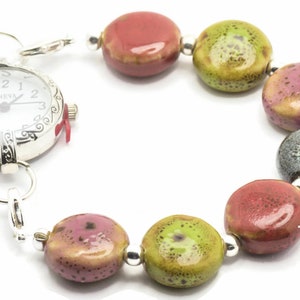 May include: A silver pocket watch with a white face and black Roman numeral markings is attached to a bracelet made of colourful ceramic beads. The beads are red, green, and grey with a speckled pattern.