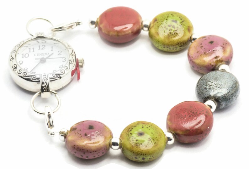 May include: A silver pocket watch with a white face and black Roman numeral markings is attached to a bracelet made of colourful ceramic beads. The beads are red, green, and grey with a speckled pattern.