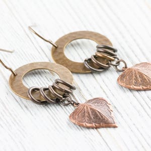 Op de afbeelding: Handgemaakte oorbellen met gehamerde messing ringen, kleine metalen ringen en koperen bladbedels. De oorbellen hebben een rustiek, door de natuur ge&iuml;nspireerd ontwerp, perfect voor dagelijks gebruik.