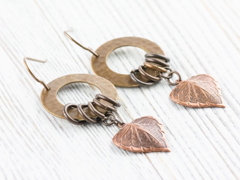 Op de afbeelding: Handgemaakte oorbellen met gehamerde messing ringen, kleine metalen ringen en koperen bladbedels. De oorbellen hebben een rustiek, door de natuur ge&iuml;nspireerd ontwerp, perfect voor dagelijks gebruik.