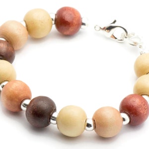 Puede incluir: Un brazalete de cuentas de madera con cierre de plata. Las cuentas son en tonos de marr&oacute;n, beige y rojo.
