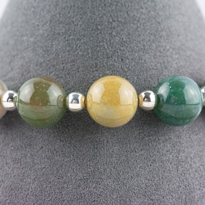 K&ouml;nnte beinhalten: Ein Armband aus runden, mehrfarbigen Edelsteinperlen mit silbernen Zwischenst&uuml;cken. Die Perlen sind in Gr&uuml;n-, Gelb- und Braunt&ouml;nen gehalten.