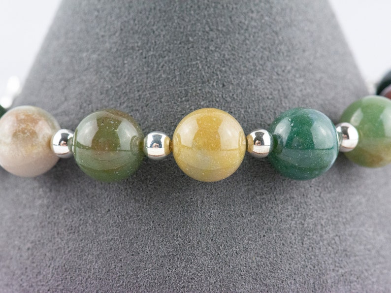 K&ouml;nnte beinhalten: Ein Armband aus runden, mehrfarbigen Edelsteinperlen mit silbernen Zwischenst&uuml;cken. Die Perlen sind in Gr&uuml;n-, Gelb- und Braunt&ouml;nen gehalten.