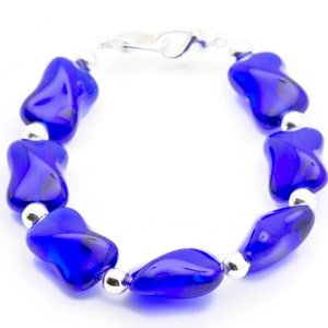 Pode incluir: Um bracelete de contas de vidro azul com detalhes prateados. O bracelete &eacute; feito de uma s&eacute;rie de contas de vidro azul que t&ecirc;m a forma de l&aacute;grima. As contas s&atilde;o conectadas por elos prateados.