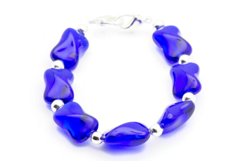 Pode incluir: Um bracelete de contas de vidro azul com detalhes prateados. O bracelete &eacute; feito de uma s&eacute;rie de contas de vidro azul que t&ecirc;m a forma de l&aacute;grima. As contas s&atilde;o conectadas por elos prateados.