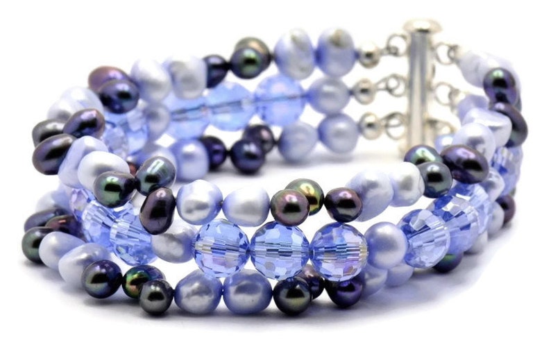 May include: A multi-strand bracelet featuring a mix of blue and black beads. The bracelet is made with glass and pearl beads, and has a silver clasp.
