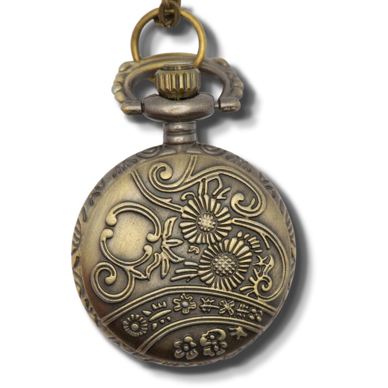 Puede incluir: Un reloj de bolsillo dorado con un dise&ntilde;o floral ornamentado en la parte delantera. El reloj tiene una cadena unida a la parte superior.