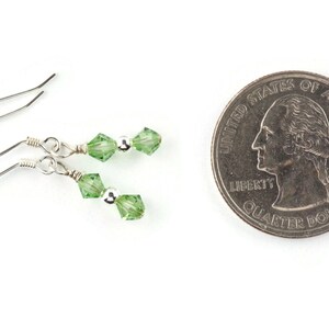 May include: A pair of silver earrings with two green crystal beads on each earring. The earrings are shown next to a US quarter for size comparison.