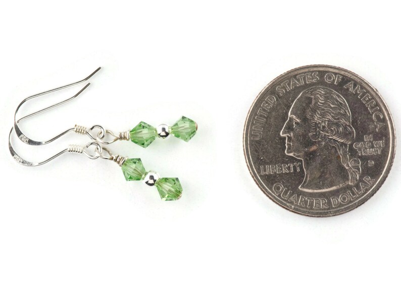 May include: A pair of silver earrings with two green crystal beads on each earring. The earrings are shown next to a US quarter for size comparison.