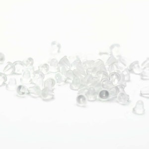 May include: A pile of clear plastic earring backs. The backs are small and round, with a slight lip around the edge.