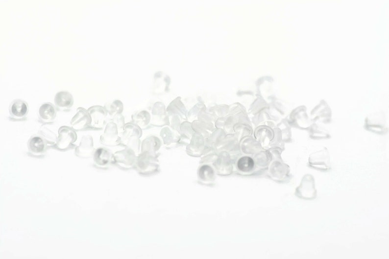 May include: A pile of clear plastic earring backs. The backs are small and round, with a slight lip around the edge.