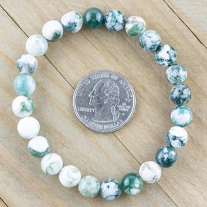 May include: A green and white agate stone beaded bracelet. The bracelet is made of round beads and is approximately the size of a US quarter.