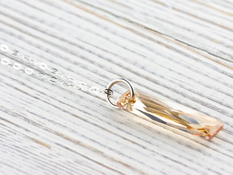 May include: A silver chain necklace with a light brown crystal pendant. The pendant is a long, rectangular shape with a faceted design.