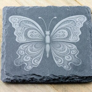 May include: A black slate coaster featuring a white, intricately designed butterfly etched into the surface.