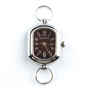 May include: Silver-toned Geneva watch with a rectangular face and a dark brown dial. The watch features white numerals and hands, with a small crown on the side. Includes two key rings for attachment.