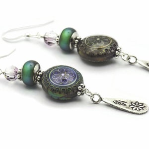 May include: A pair of silver earrings with a green iridescent bead, a purple and silver patterned bead, and a silver teardrop charm with a flower design.