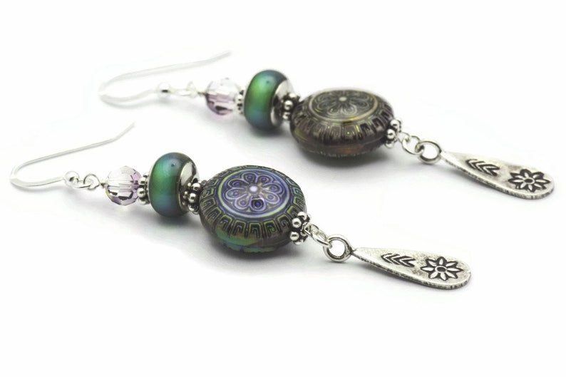 May include: A pair of silver earrings with a green iridescent bead, a purple and silver patterned bead, and a silver teardrop charm with a flower design.