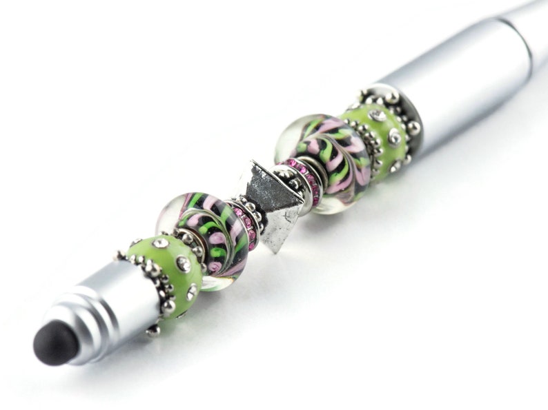 K&ouml;nnte beinhalten: Ein silberner Stift mit schwarzer Spitze und gr&uuml;nen und rosa Glasperlen. Die Perlen sind mit silbernen Akzenten und Strasssteinen verziert.