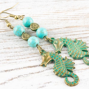 May include: A pair of turquoise and bronze earrings featuring seahorse charms and turquoise beads.