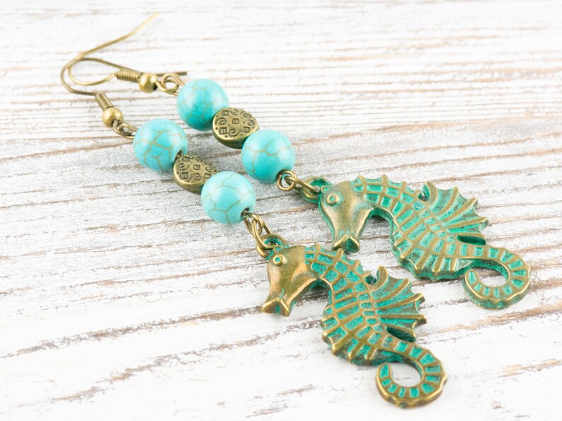 May include: A pair of turquoise and bronze earrings featuring seahorse charms and turquoise beads.